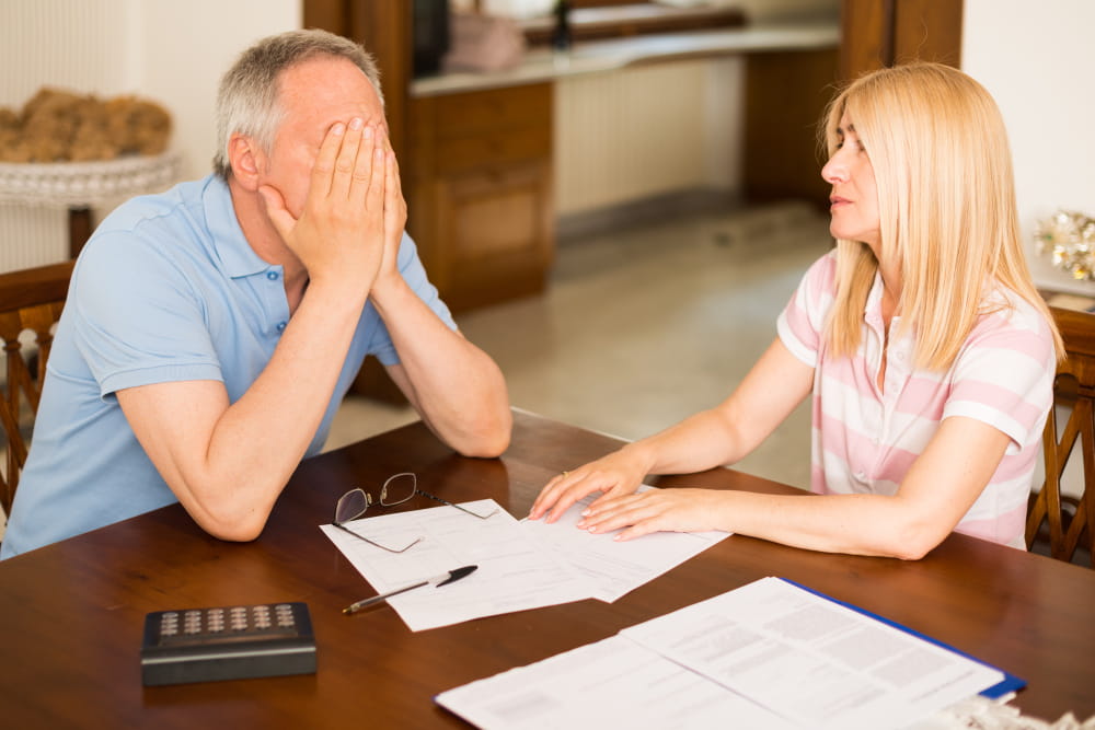 Un couple stressé discutant de documents financiers à une table de salle à manger en présence de leur avocat de divorce.